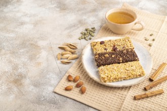 Granola bars with caramel, nuts, flakes in ceramic plate on brown concrete background, beige linen