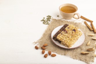 Granola bars with caramel, nuts, flakes in ceramic plate on white wooden background, beige linen