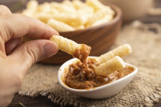 Corn flakes sticks with caramel in wooden bowl with hand on brown wooden background and linen