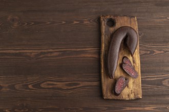 Sujuk sausage on wooden cutting board with pepper and herbs on brown wooden background. Top view,