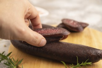 Sujuk sausage with hand on wooden cutting board with pepper and herbs on brown concrete background.