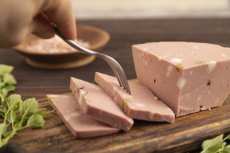 Mortadella sausage with hand on wooden cutting board with pepper and herbs on brown wooden
