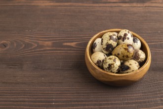 Pile of raw Quail eggs in bowl on a brown wooden background. side view, copy space