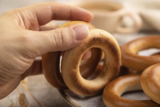 Homemade Ring Bagel with hand with cup of coffee on brown concrete background and linen textile.