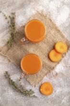 Two glasses with carrot juice, on brown concrete background and linen textile. Diet, healthy eating
