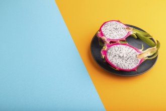 Ripe Pitaya on blue plate on blue and orange pastel paper background, side view, copy space,