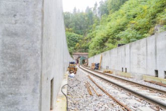 Blick auf Eisenbahngleise, die zu einem Tunnel führen, flankiert von massiven Betonwänden, Bau der