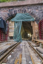 Ansicht eines Tunnels mit sichtbaren Schienen und Baugerüst, beleuchtet durch Baustellenlampen, Bau