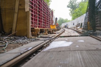 Baustelle mit Schienen und Holzbrettern in einem Waldgebiet, von Kabeln und Konstruktionsmaterial
