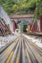 Tunnel im Bau mit langen Metallstangen und umliegenden Betonwänden in einer von Bäumen umgebenen