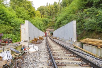 Eisenbahnschienen führen zu einem Tunnel, umgeben von Baustellenmaterialien und Wald, Bau der
