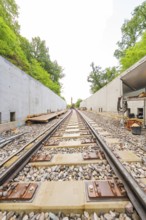 Eisenbahngleise zwischen Betonwänden führen in die Ferne, umgeben von Wald, Bau der Hermann