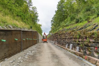 Baggerarbeiten in einer grünen Landschaft zwischen steilen, bewachsenen Hängen, Bau der Hermann