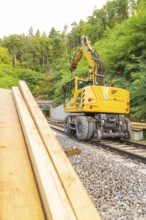 Gelbes Baufahrzeug mit Kran auf Schienen in waldreicher Umgebung, Bau der Hermann Hessenahn, Calw,