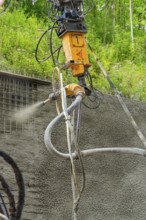 Nahaufnahme einer Maschine, die Beton auf eine Struktur sprüht, umgeben von grüner Vegetation, Bau