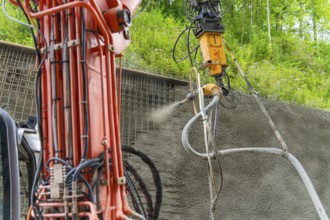 Detailaufnahme einer Maschine beim Auftragen von Spritzbeton vor grüner Kulisse, Bau der Hermann