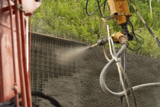 Spritzbeton wird maschinell auf ein Gitter an einem Hang aufgetragen, Bau der Hermann Hessenahn,