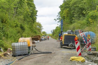 Baustellenszene mit Maschinen und Geräten entlang einer Straße in bewaldetem Gebiet, Bau der