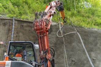 Maschine sprüht Beton an einer Wand entlang eines bewachsenen Bauplatzes, Bau der Hermann