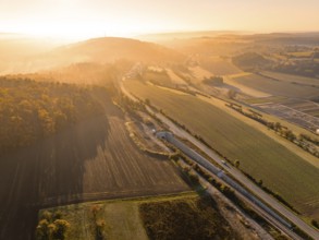 Eine von Sonnenlicht durchflutete Talansicht mit Feldern, Hügeln und Straßen bei Sonnenaufgang,