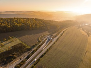 Panorama einer Landschaft in der Dämmerung mit Eisenbahn und Straße neben Feldern und bewaldeten