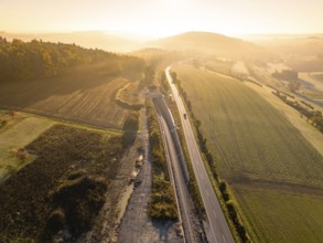 Ein Sonnenuntergang über einer ländlichen Landschaft mit Eisenbahn und Straße, umgeben von Feldern