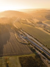 Landschaft während eines Sonnenaufgangs mit Feldern, Hügeln und einer Straße, die von goldenem