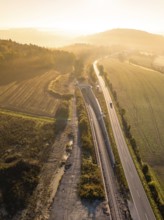 Luftaufnahme einer Landschaft im Sonnenlicht mit Eisenbahnlinie und Straße, umgeben von Feldern und