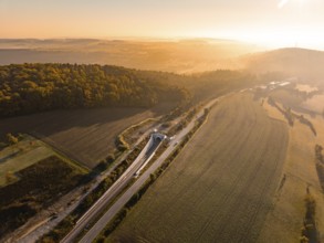 Panoramablick über eine hügelige Landschaft mit Feldern und einer Straße im goldenen Sonnenlicht,