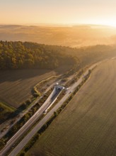 Luftaufnahme einer Landschaft mit Feldern, Hügeln, einer Straße und einer Eisenbahnlinie bei