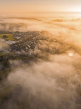 Vernebelte Luftaufnahme eines Dorfs in der Morgendämmerung in warmem Orange und Braun, Gechingen,