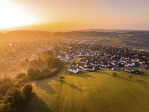Luftaufnahme eines sonnigen Dorfs bei Sonnenuntergang mit umliegenden Feldern und Bäumen,