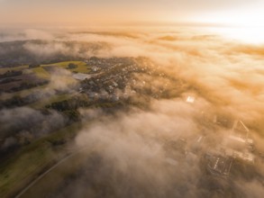Luftaufnahme eines Dorfes im Nebel mit warmem Morgenlicht, die Landschaft wirkt weich, Gechingen,