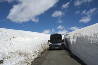 Van zwischen hohen Schneewehen auf einer Bergstraße unter klarem Himmel, mit dem Camper zum Aragaz,
