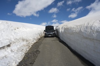 Van auf schmaler Straße zwischen hohen Schneemauern mit blauem Himmel, mit dem Camper zum Aragaz,