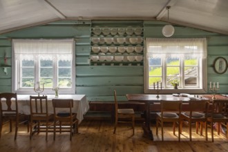 Esszimmer mit Holztischen, Holzstühlen und Tellern in einem Regal, historischer Bauernhof und