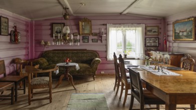 Wohnzimmer mit antiken Holzmöbeln und dekorativen Bildern an einer rosa gestrichenen Wand,
