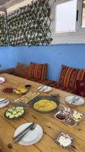 Rustic wooden table features a spread of moroccan breakfast food, with a pan of omelette,
