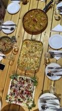 Table set for a dinner party with a large paella of shrimp, baked vegetable gratin and a vibrant