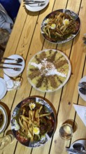 Table spread of moroccan dishes for sharing, chicken tajine topped with fries and eggs, sweet seffa