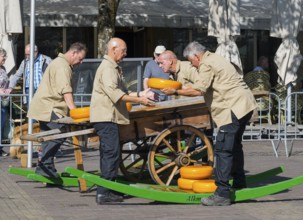 Männer in beiger Kleidung stapeln Käseräder auf einem traditionellen Holzwagen, Käse, Käsemarkt,