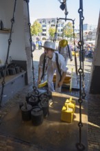 Ein Mann in historischer Kleidung wiegt Käse auf einem alten Markt mit anderen Teilnehmern,