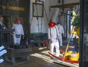 Männer in traditioneller Kleidung transportieren Käse in einem geschlossenen Raum, ehemalige