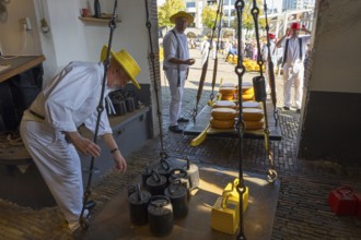 Männer in traditioneller Kleidung wiegen Käseräder auf einem historischen Markt, ehemalige