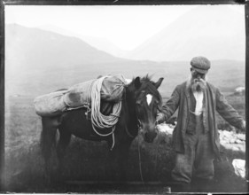 Old man with pack horse carrying mountaineering equipment, thought to be Cuillin mountains, Skye,