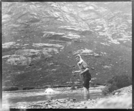 Person crawling across river stream secured by man holding a rope mountain exploration c 1900