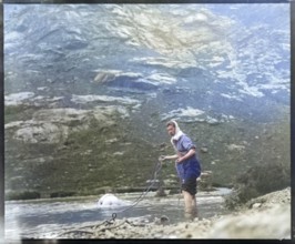 Person crawling across river stream secured by man holding a rope mountain exploration c 1900