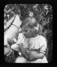 Halftone portrait photograph of young girl holding and looking at her cuddly toy c 1900
