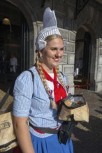 Smiling woman in traditional traditional costume with traditional headgear in front of a historic