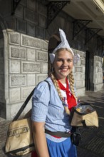 Woman in traditional dress and headdress smiling in front of a historic building, former city weigh